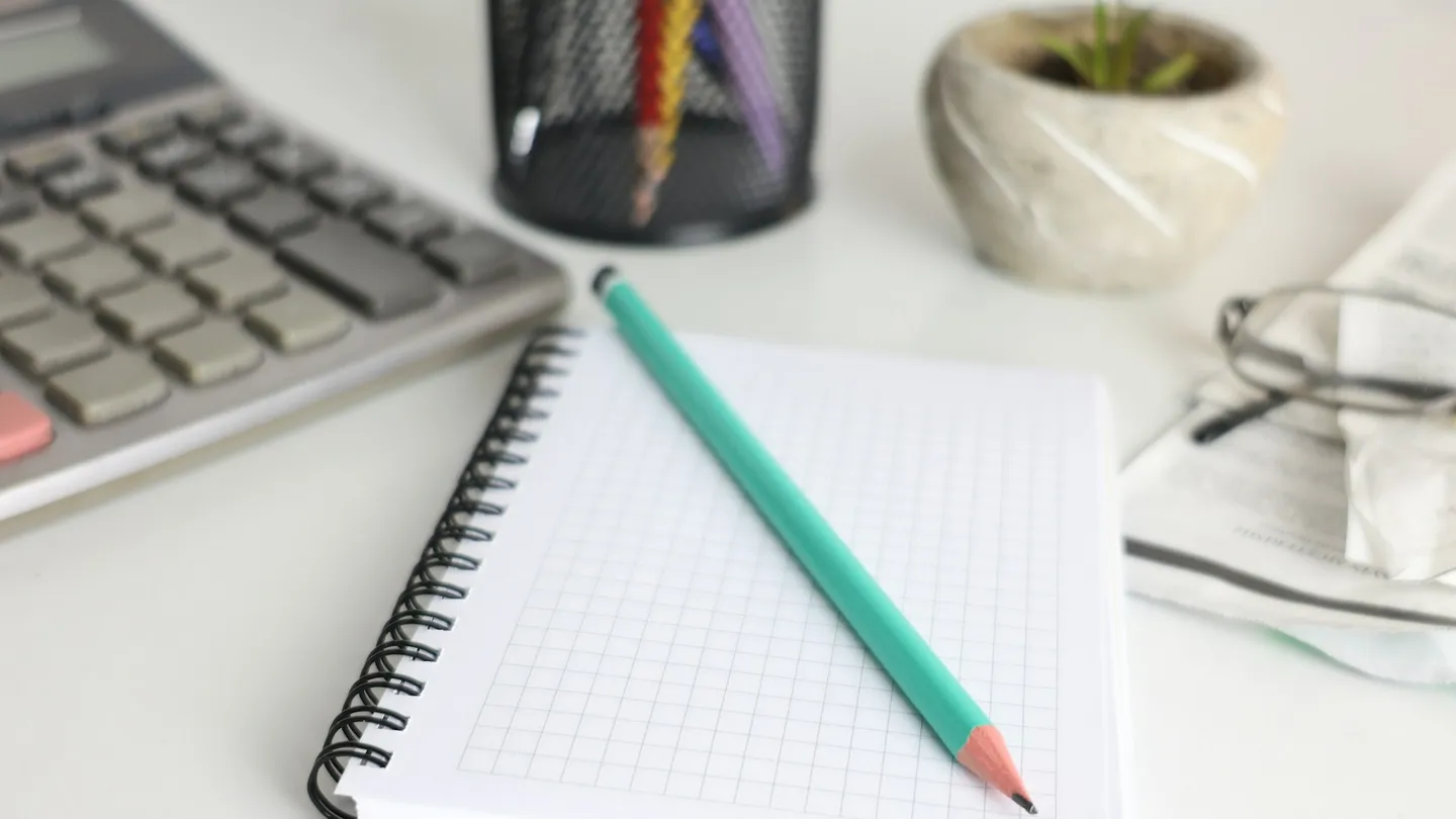 Desk with calculator, notebook, pencil, and plant