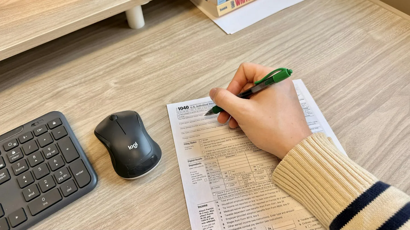 Hand writing on document next to keyboard and mouse