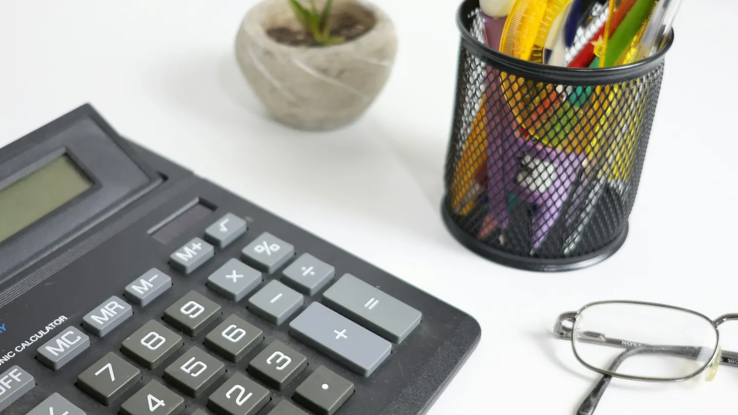 Calculator, glasses, and pens on a white desk