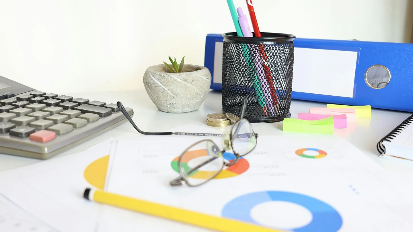Desk with calculator, glasses, charts, and office supplies