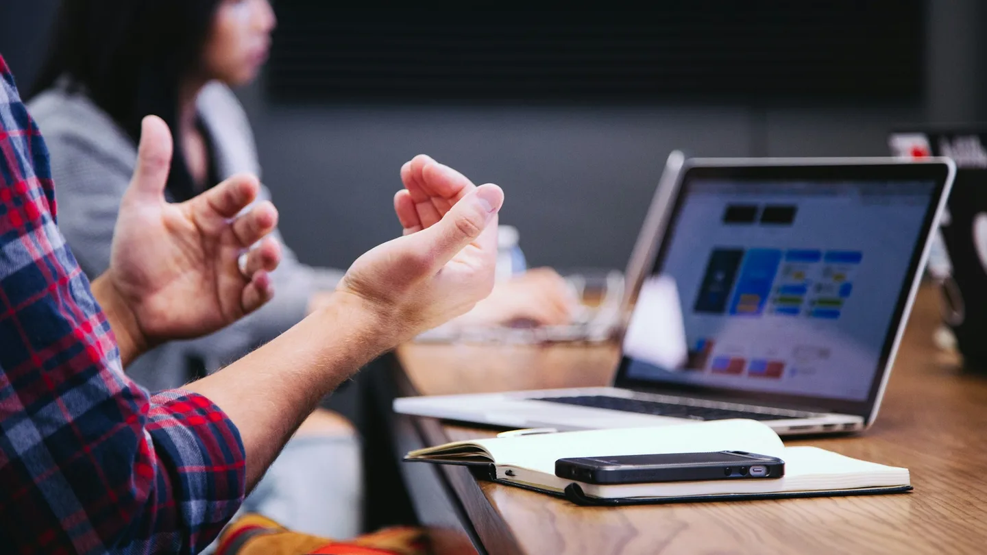 person gesturing during meeting with laptop
